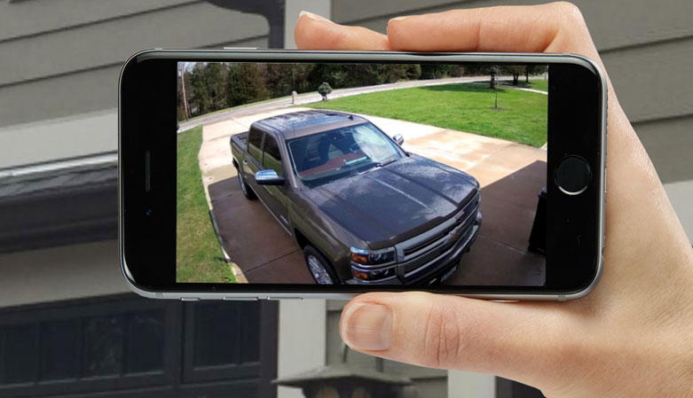person looking at mobile phone and security cameras with car in driveway