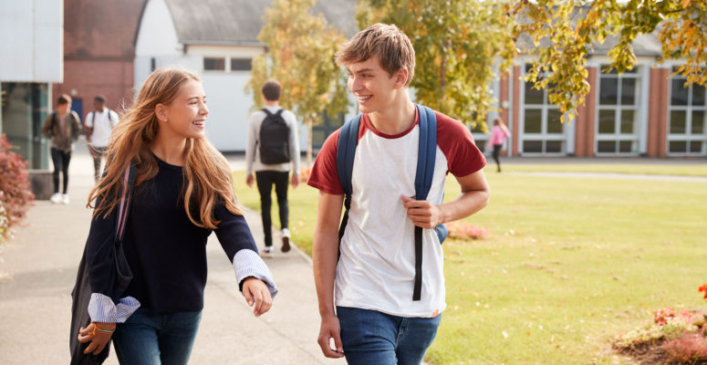 Teenage Students Walking across College Campus wearing backpacks