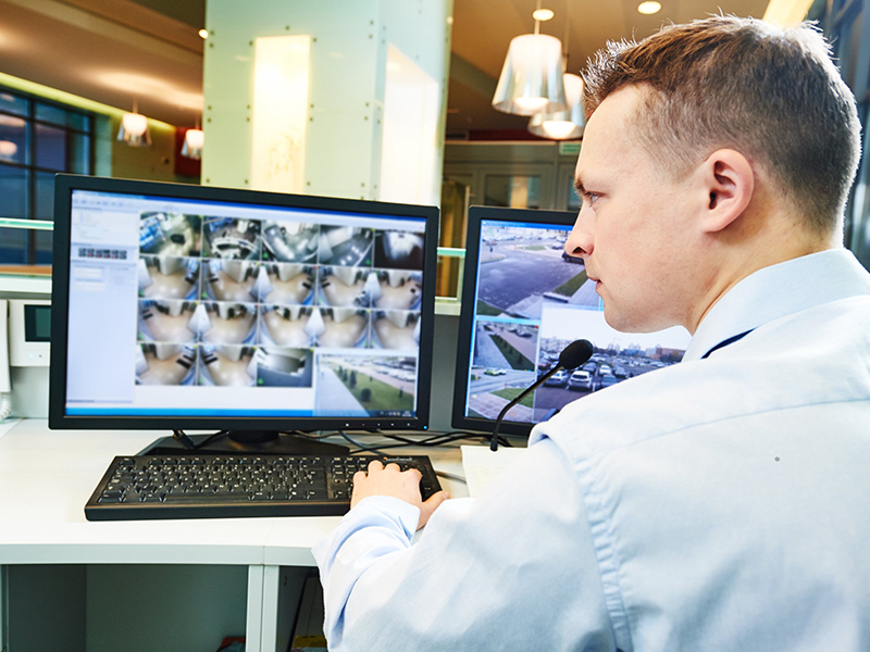 Security Guard Looking at Video Surveillance Monitor in Burglar Alarm Monitoring Station